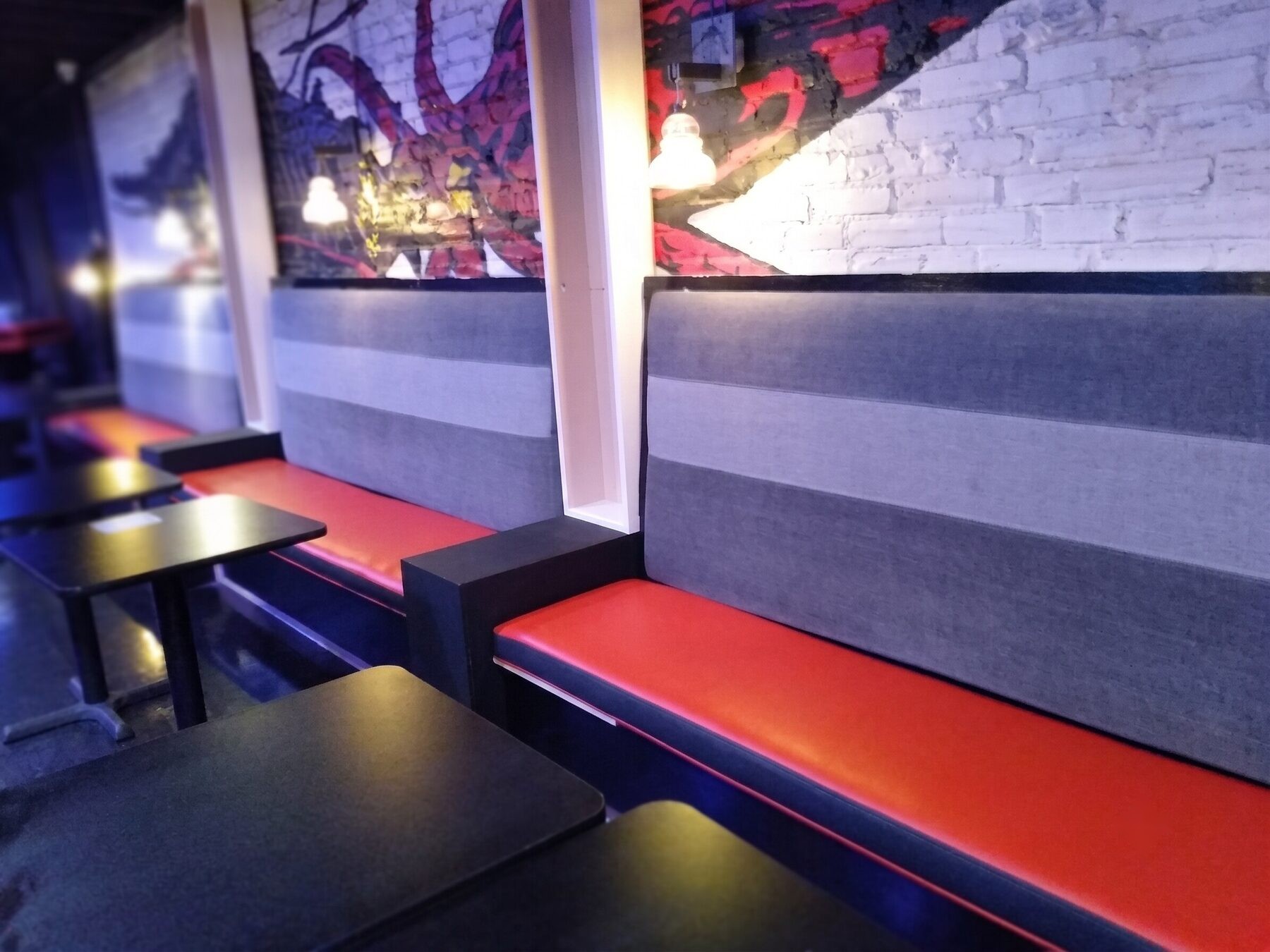 Booth seating with gray tweed backs and red vinyl seats beneath a mural in a bar