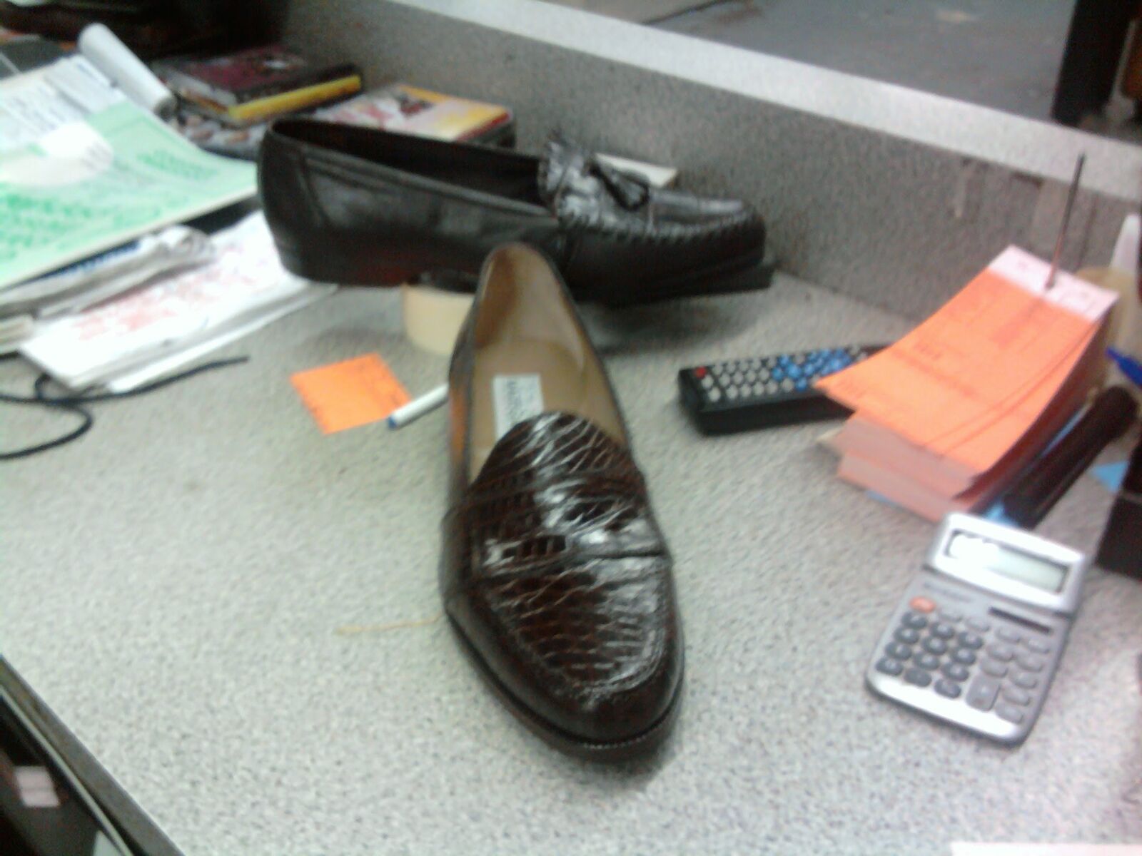 Pair of dark brown crocodile loafers on the counter, tagged and in for repair