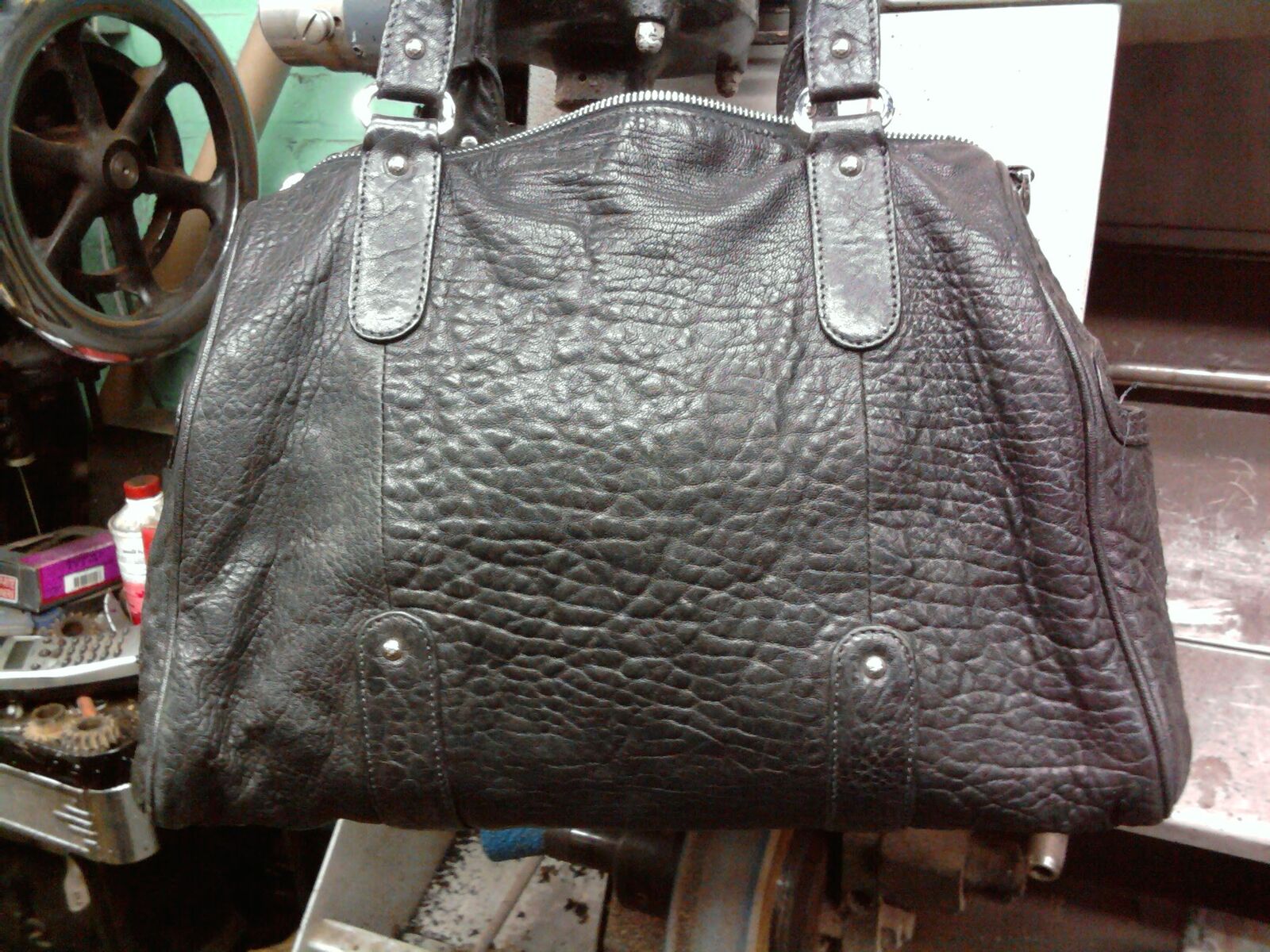 Black pebbled leather handbag hanging in the workshop, stitching machines behind