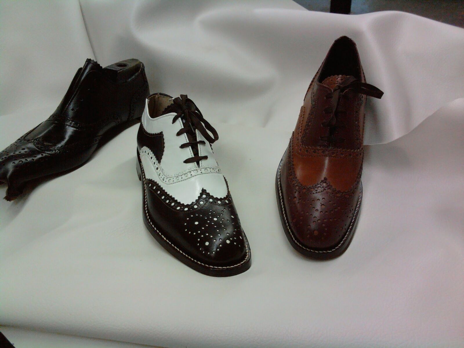 Three handmade full-brogue wingtips in dark brown, brown-and-white spectator, and cognac, on white leather