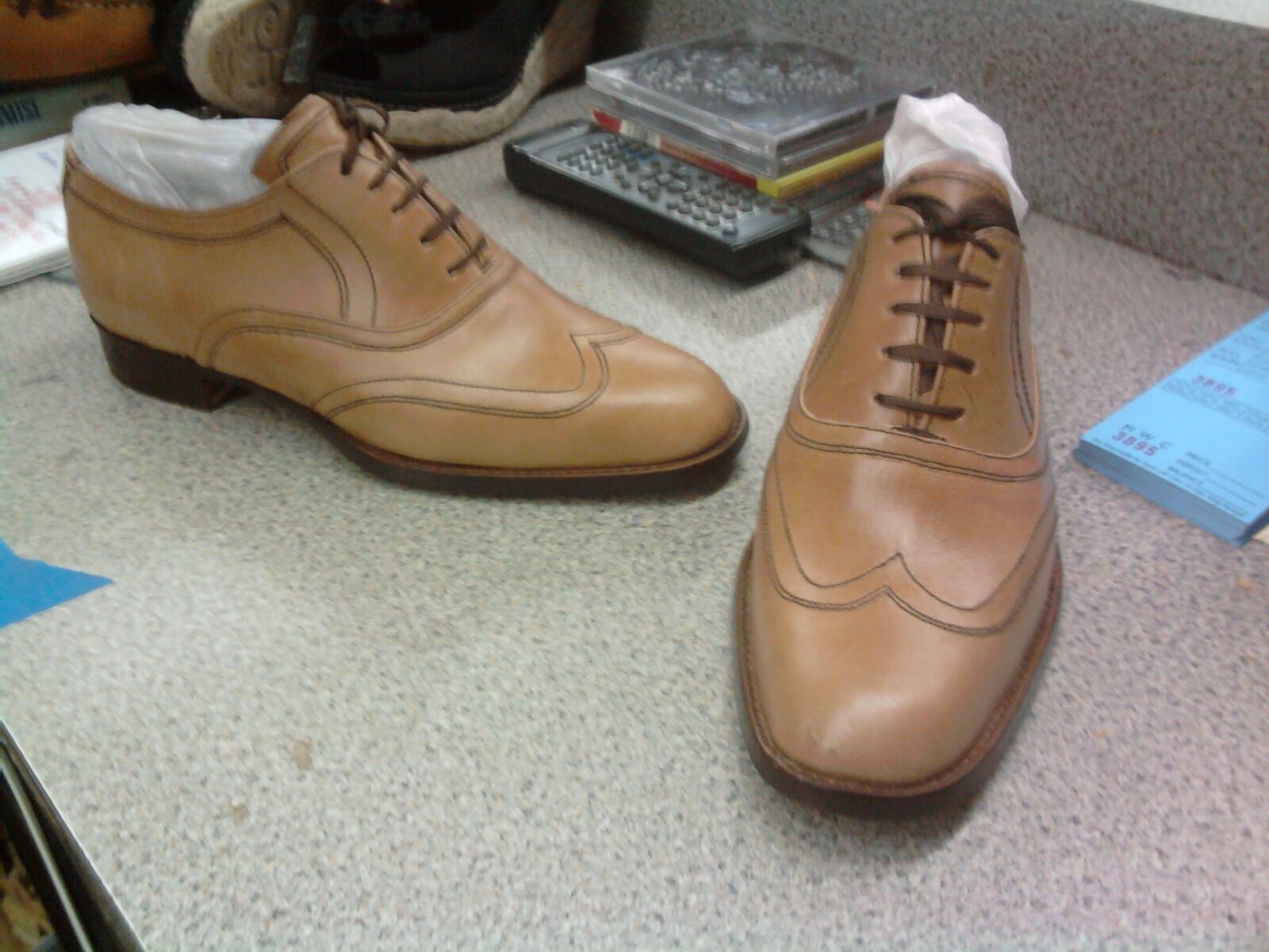 Pair of handmade tan leather wingtip oxfords with tonal stitching, one still stuffed with tissue